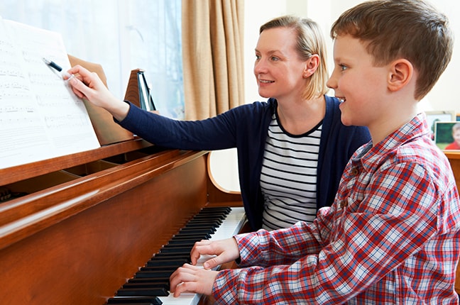 Professora ensinando seu aluno a tocar piano e gravar aula online