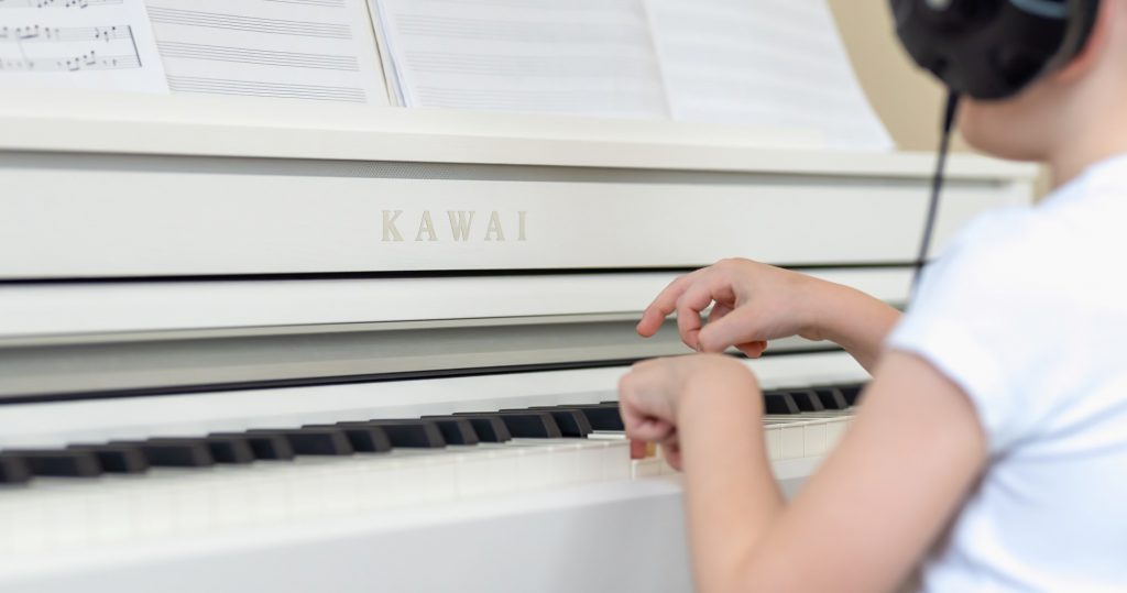 Criança tocando piano branco da Kawai