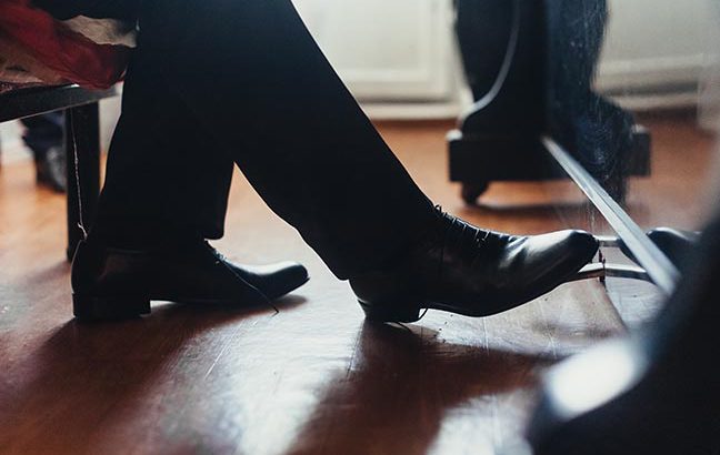 A male musician plays the piano, presses the foot in black shoes on the pedal close-up. Photography, concept.