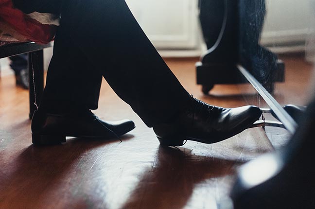 A male musician plays the piano, presses the foot in black shoes on the pedal close-up. Photography, concept.