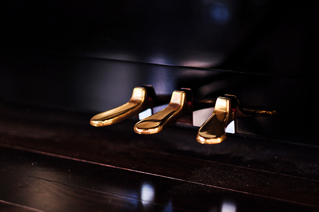 Brass piano pedals. Three in a row. Shining vintage metallic texture in a dark background and against wooden floor. Close up and selective focus.